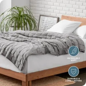 Grey weighted blanket spread across a bed in a bright bedroom