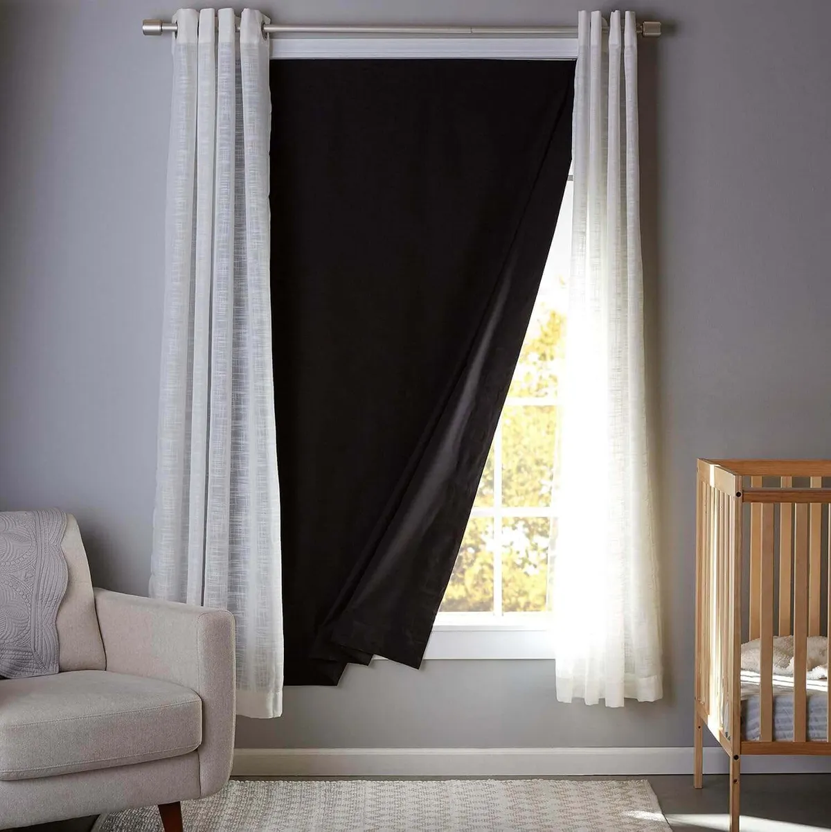 Blackout curtain covering a nursery window beside a sheer white curtain