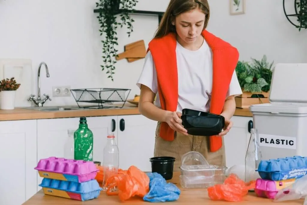 Woman sorting plastic bottles and cartons into recycling bins in a kitchen