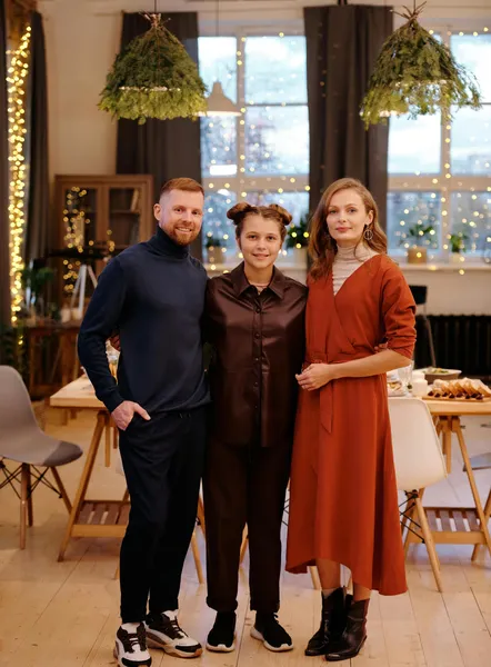 Three people in autumn-toned outfits standing in a decorated dining room
